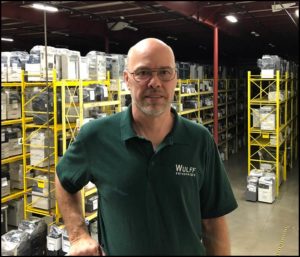 Jerry, Domestic Sales Manager, in Warehouse filled with shelves of copiers & office equipment.